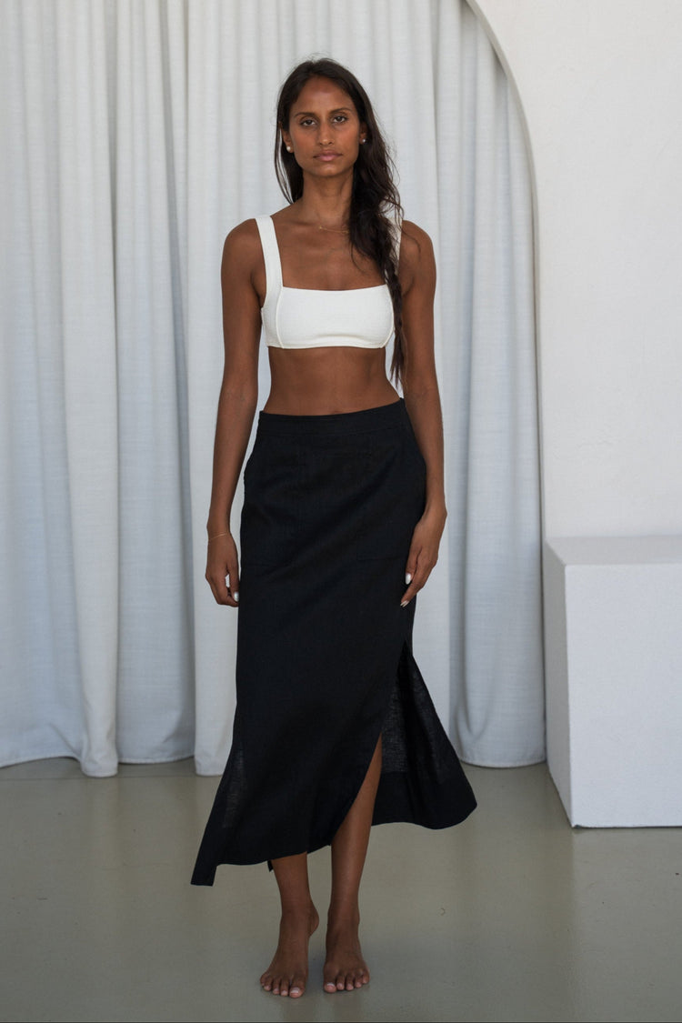 Nadi Linen Midi Skirt in Black - front view, styled with a white top, white curtain background - Lilly Pilly Collection