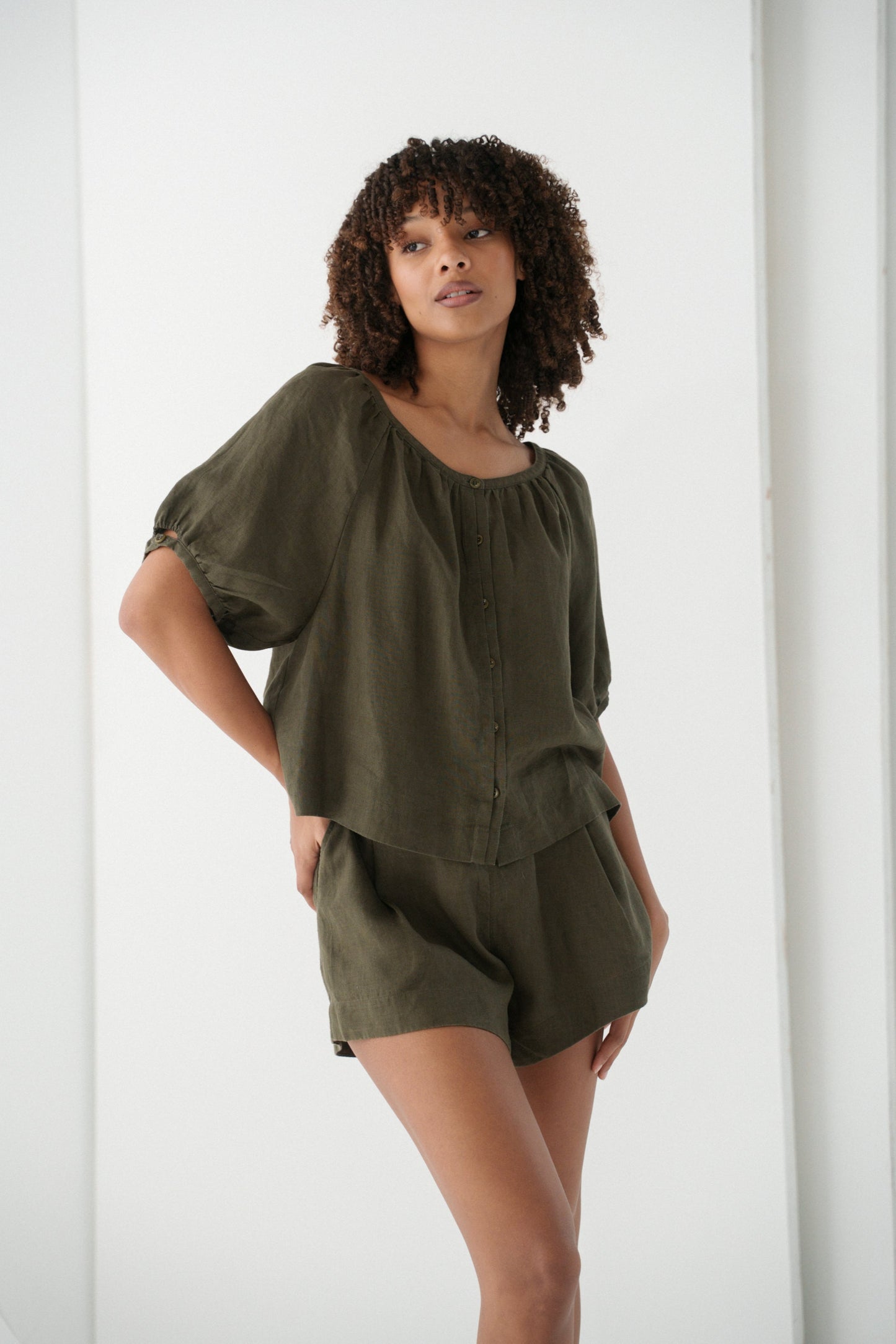 LILLY PILLY woman wearing a khaki Pia linen shirt top and Gaia shorts with a white curtain background