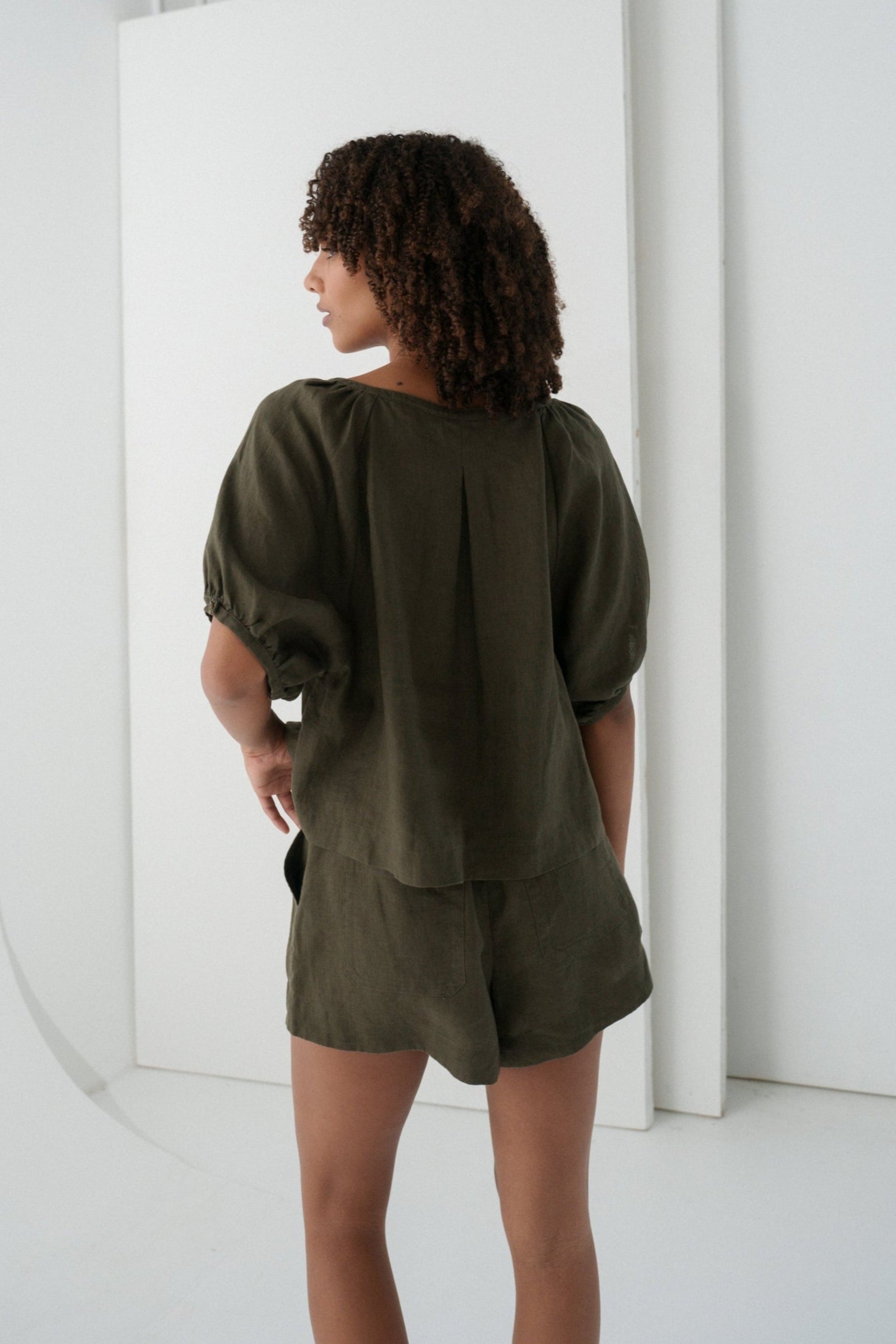 LILLY PILLY woman wearing a khaki Pia linen shirt top and Gaia shorts back view standing against a white background