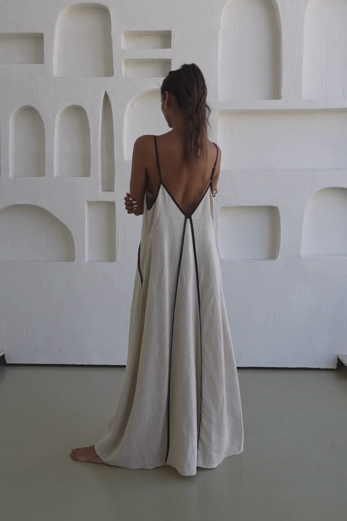 Lilly Pilly woman wearing an oatmeal Azalea dress with black straps and trim while in the studio.
