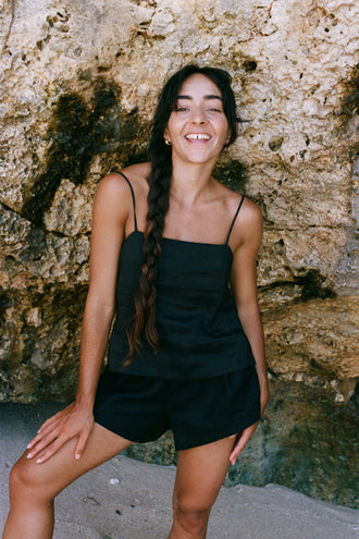 Rosa Linen Silk Cami in Black - woman laughing, square neckline and spaghetti straps, styled with matching black linen silk shorts, rocky cave backdrop - Lilly Pilly Collection