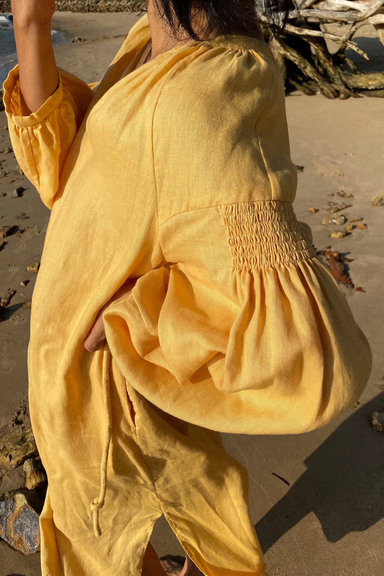 Skylar Linen Dress in Butter Yellow - side close up view while standing on the beach - Lilly Pilly Collection