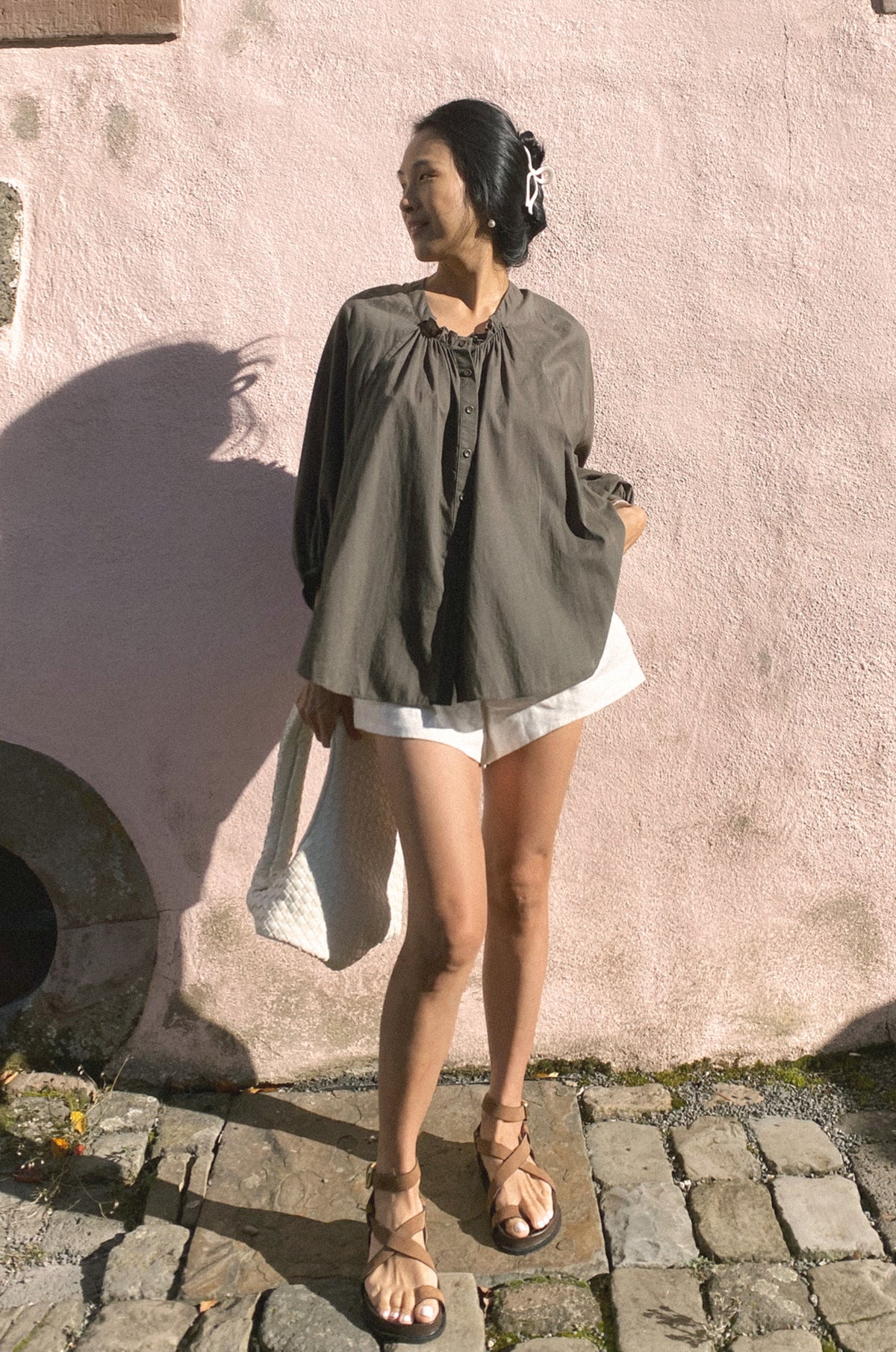 Woman standing against a textured wall wearing a green top and white shorts.