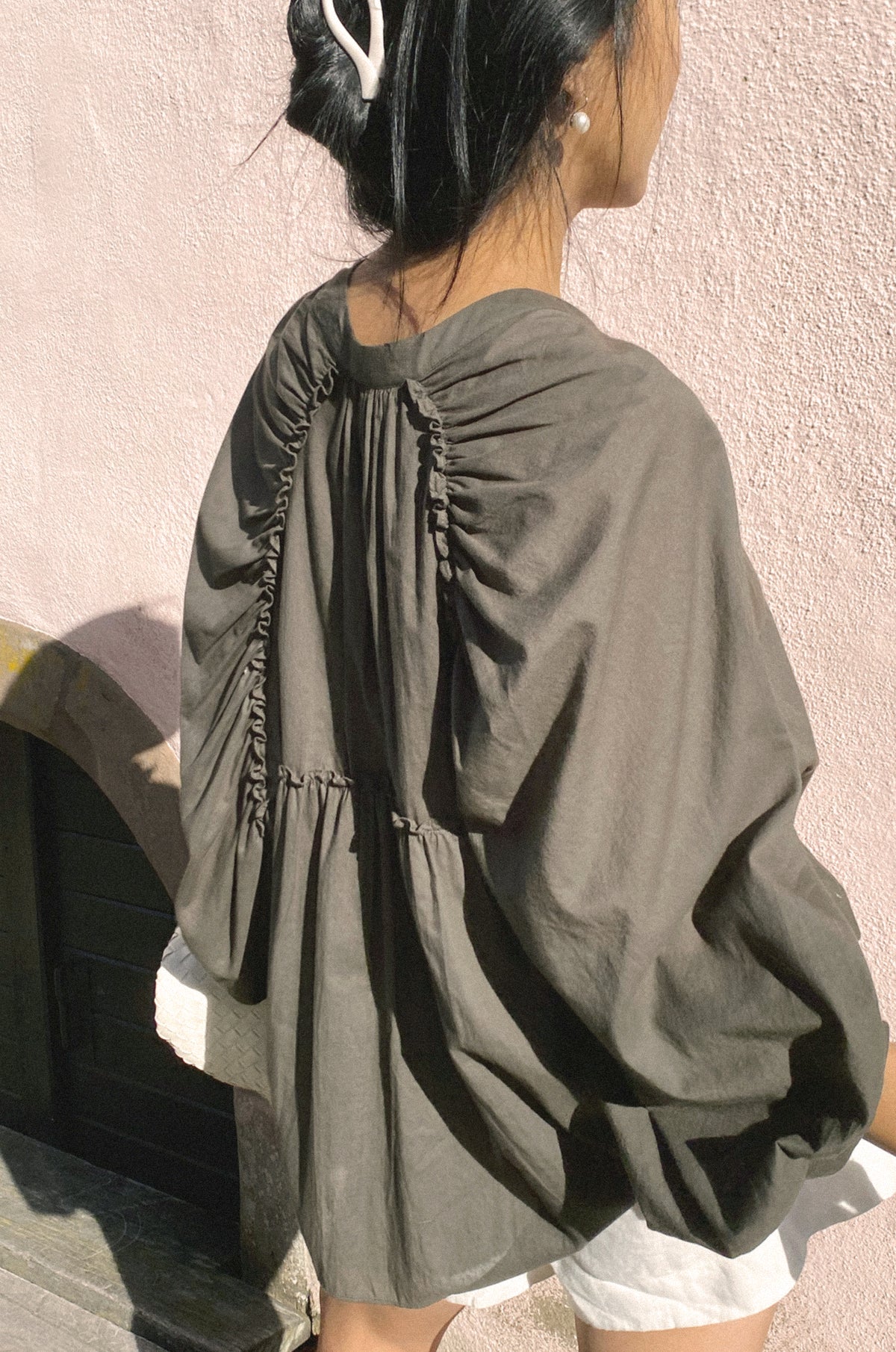 Person wearing a gray oversized shirt against a light pink wall