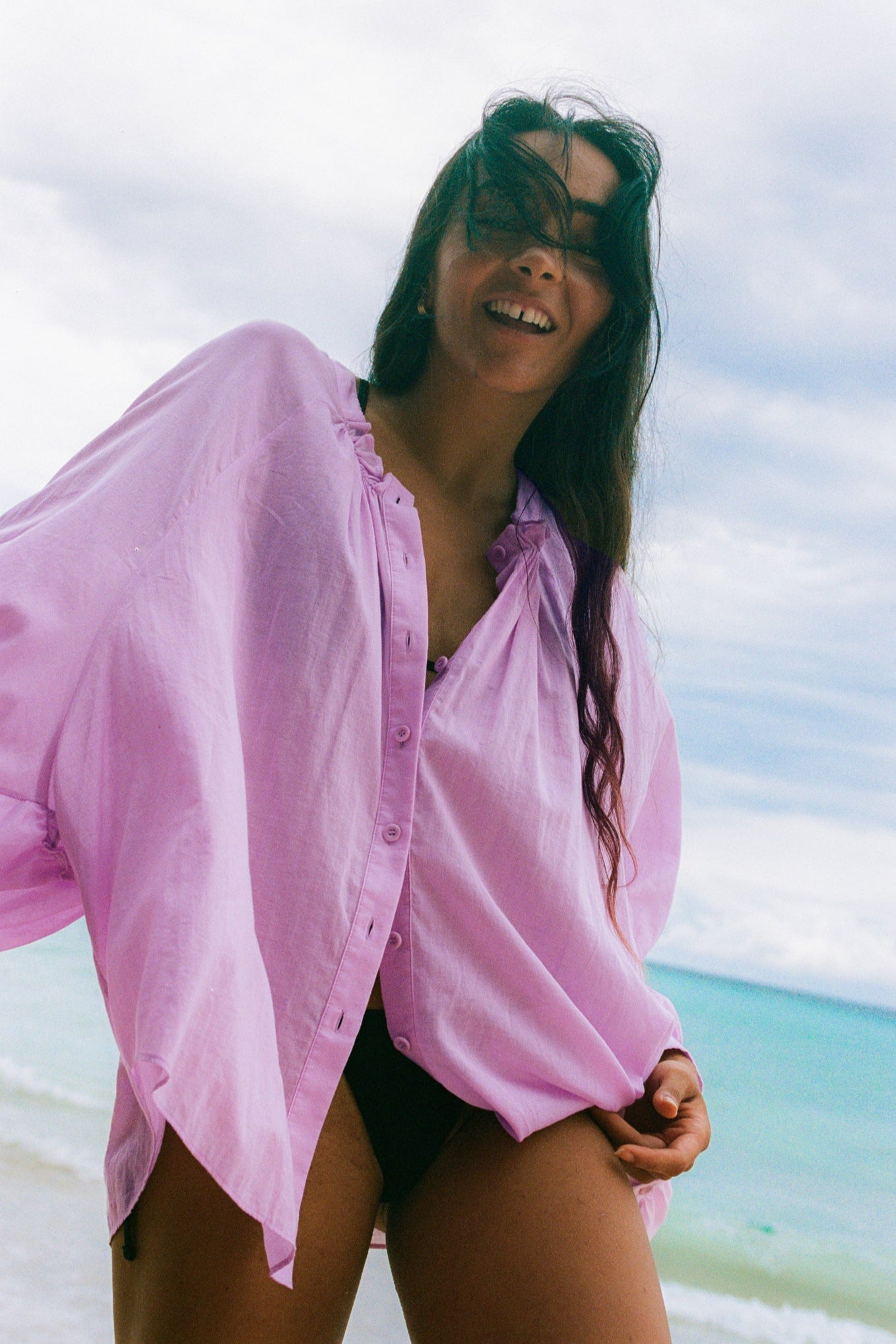 LILLY PILLY woman wearing a orchid Thalia cotton voile shirt  blouse over a black bikini on a beach